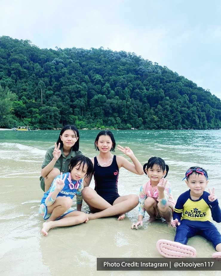 A group of kids were sitting on a sandy beach and taking a picture at Pantai Kerachut - Lexis Suites Penang