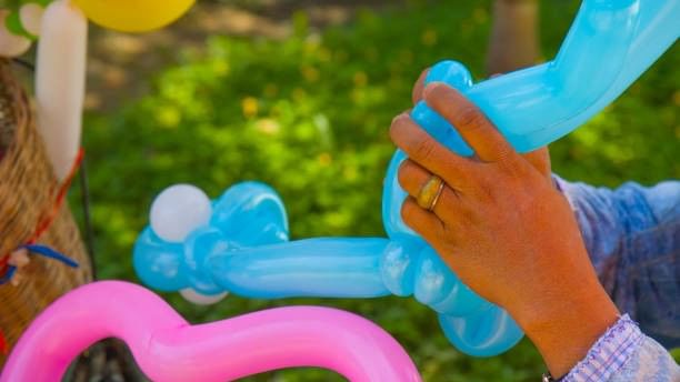 Hands twisting colorful balloons into creative shapes during Balloon Artist Fun event outdoors on green grass.
