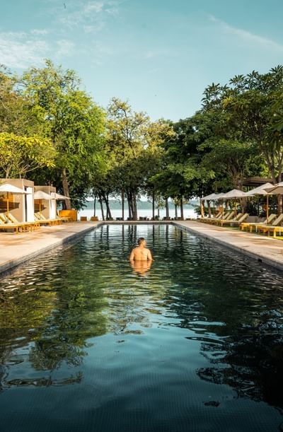 Person relaxing in an outdoor pool by trees overlooking the sea at El Mangroove Hotel