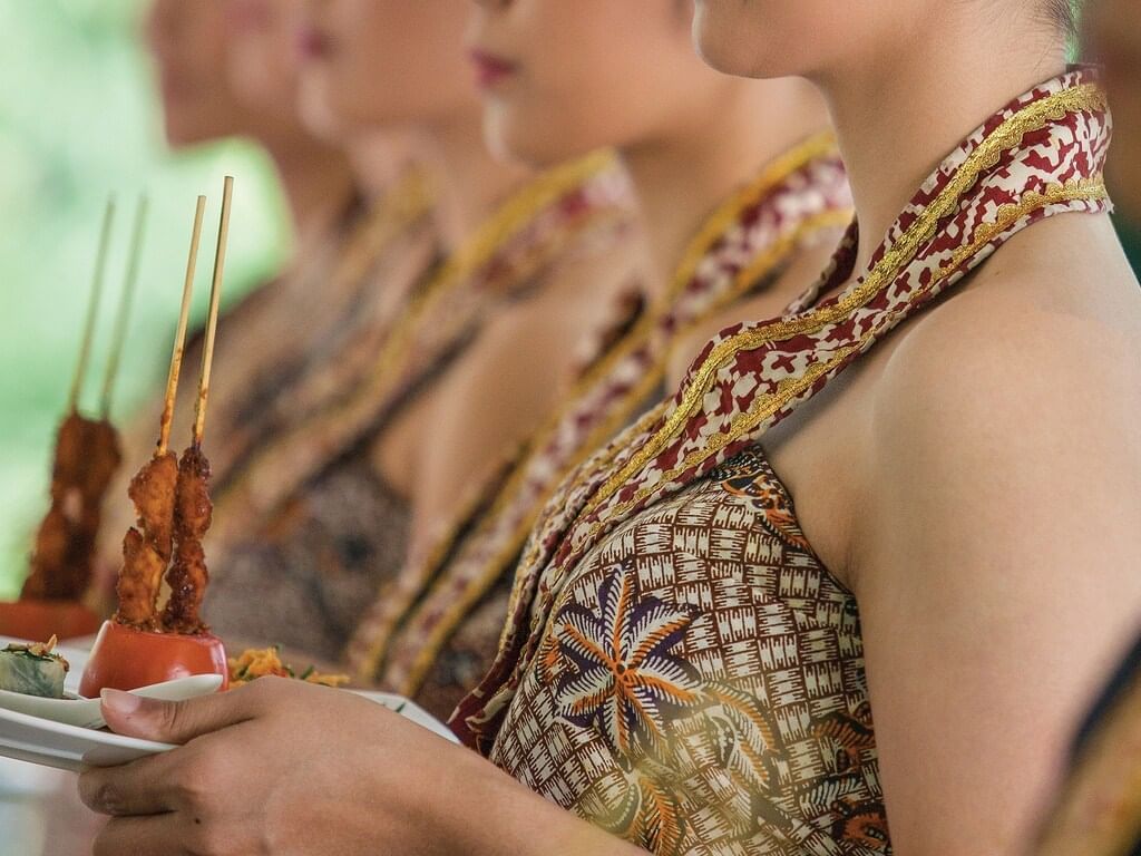 Ladies dressed in traditional clothes holding cooked meat dishes ready to serve