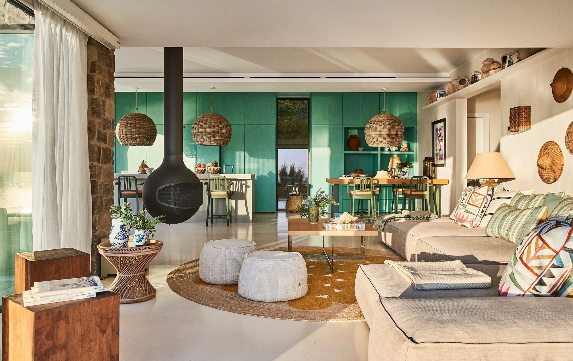 Bright, stylish living room at Marbella Club with teal cabinets, black hanging fireplace, and wicker lighting
