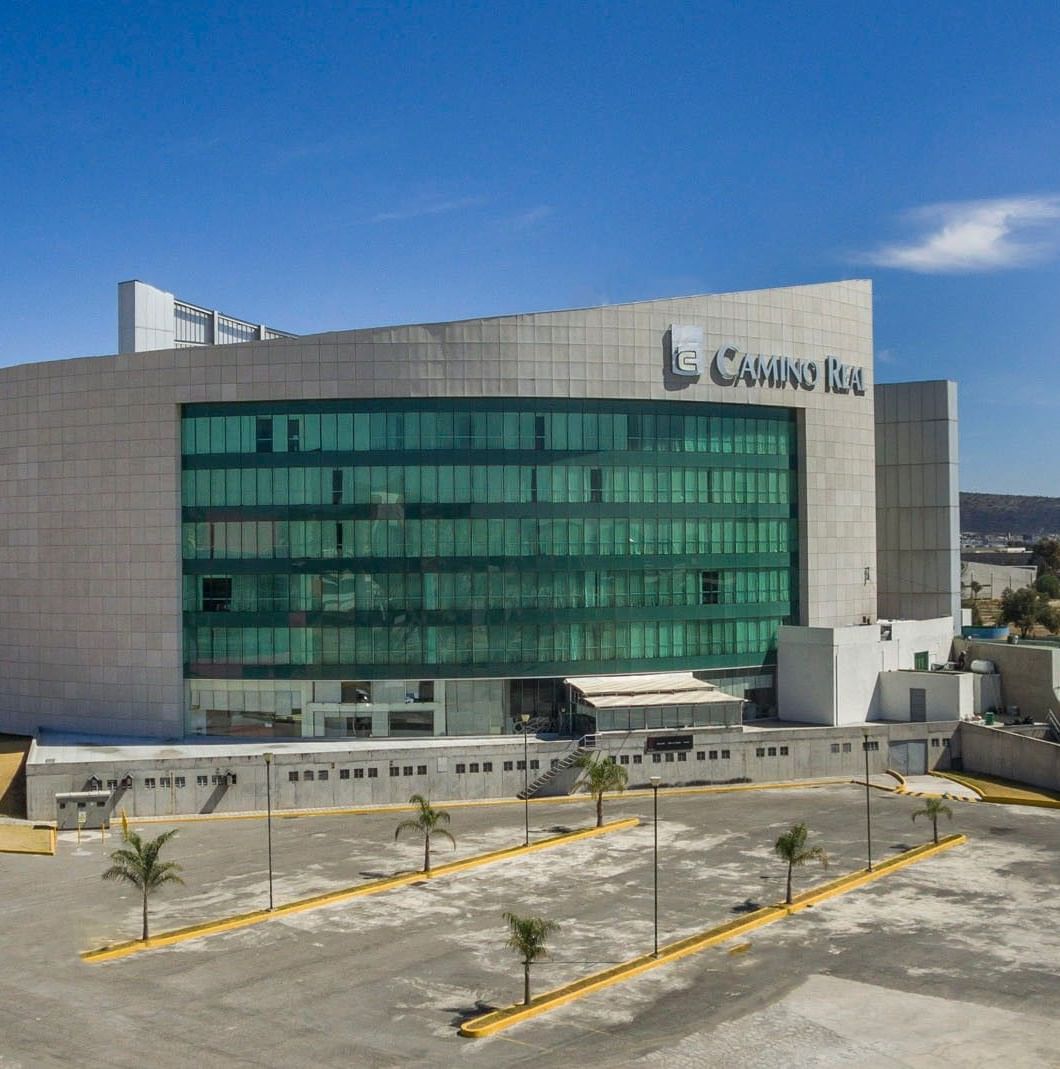 Wide aerial view of Camino Real Pachuca building during the day with a large parking lot in front