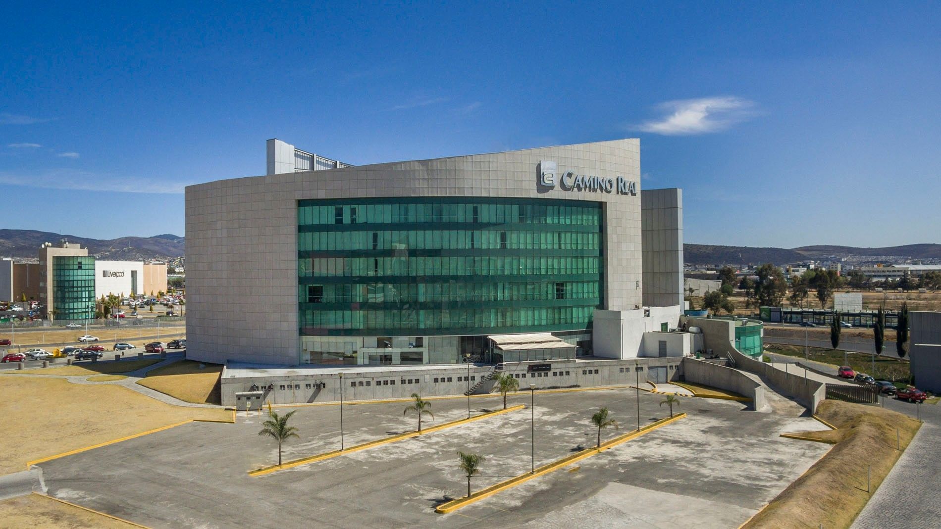 Wide aerial view of Camino Real Pachuca building during the day with a large parking lot in front