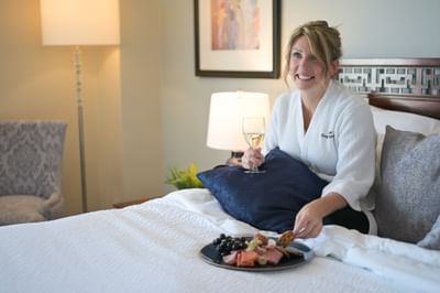 Woman in a bathrobe enjoying wine  and fresh fruits on the bed in Standard King Room at Rodd Grand Yarmouth