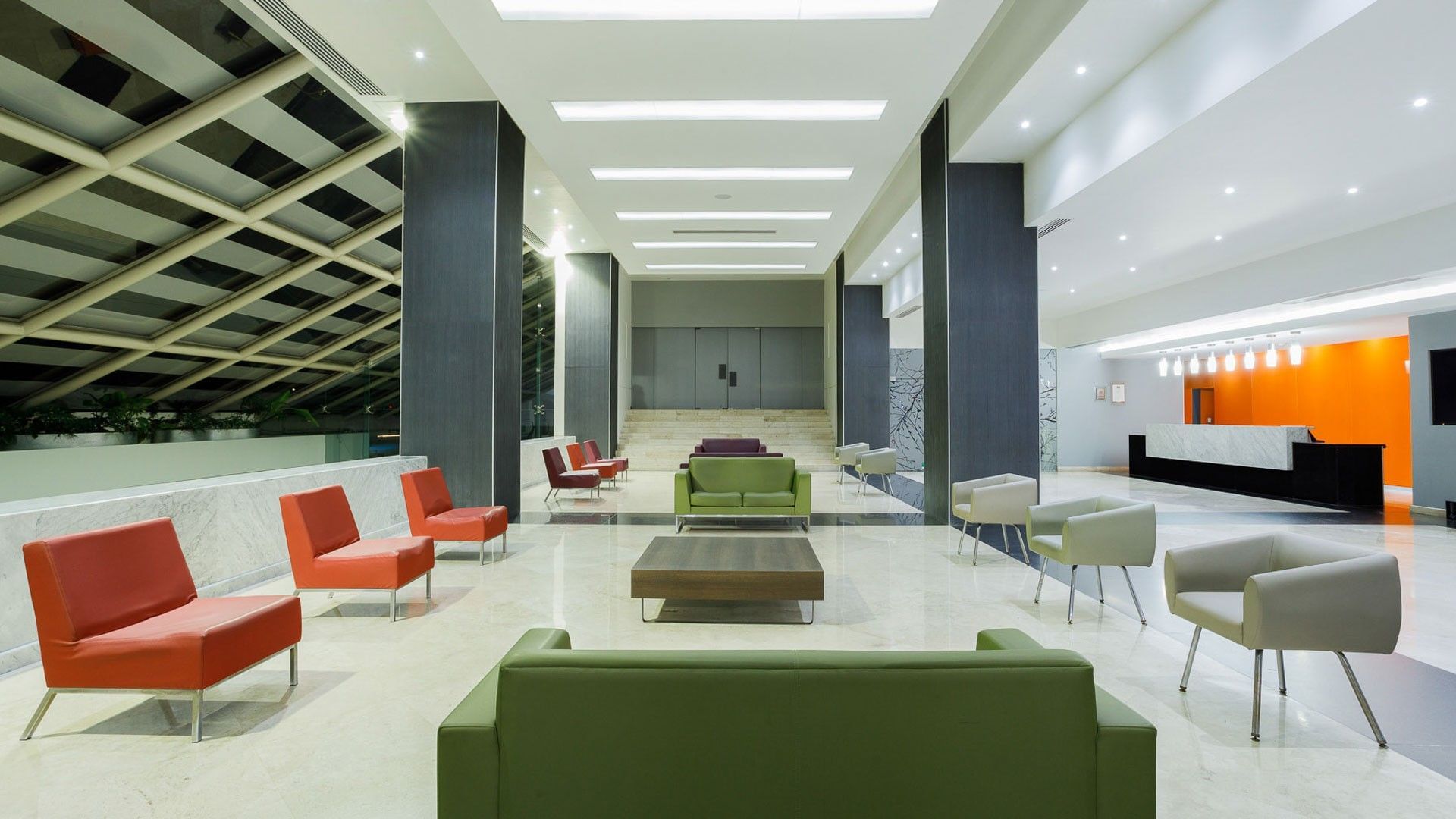 Real Inn Tijuana lobby with colorful chairs by a low table under bright lights, surrounding a spacious reception area