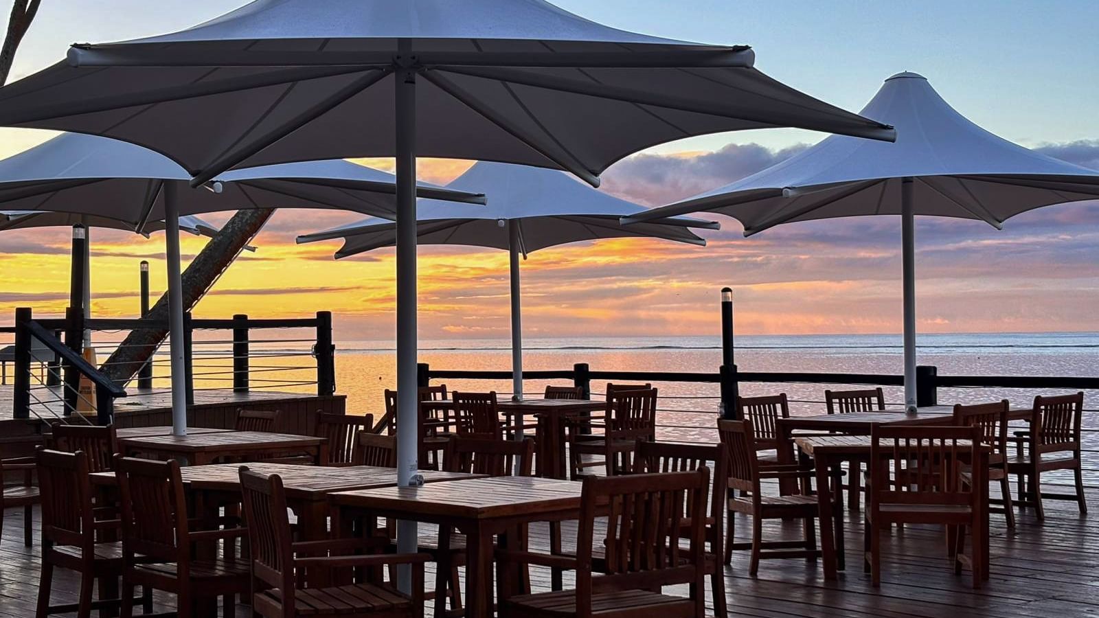 Sunset view over the ocean from a seaside restaurant with tables and umbrellas at Warwick Fiji Resort and Spa, Korolevu.