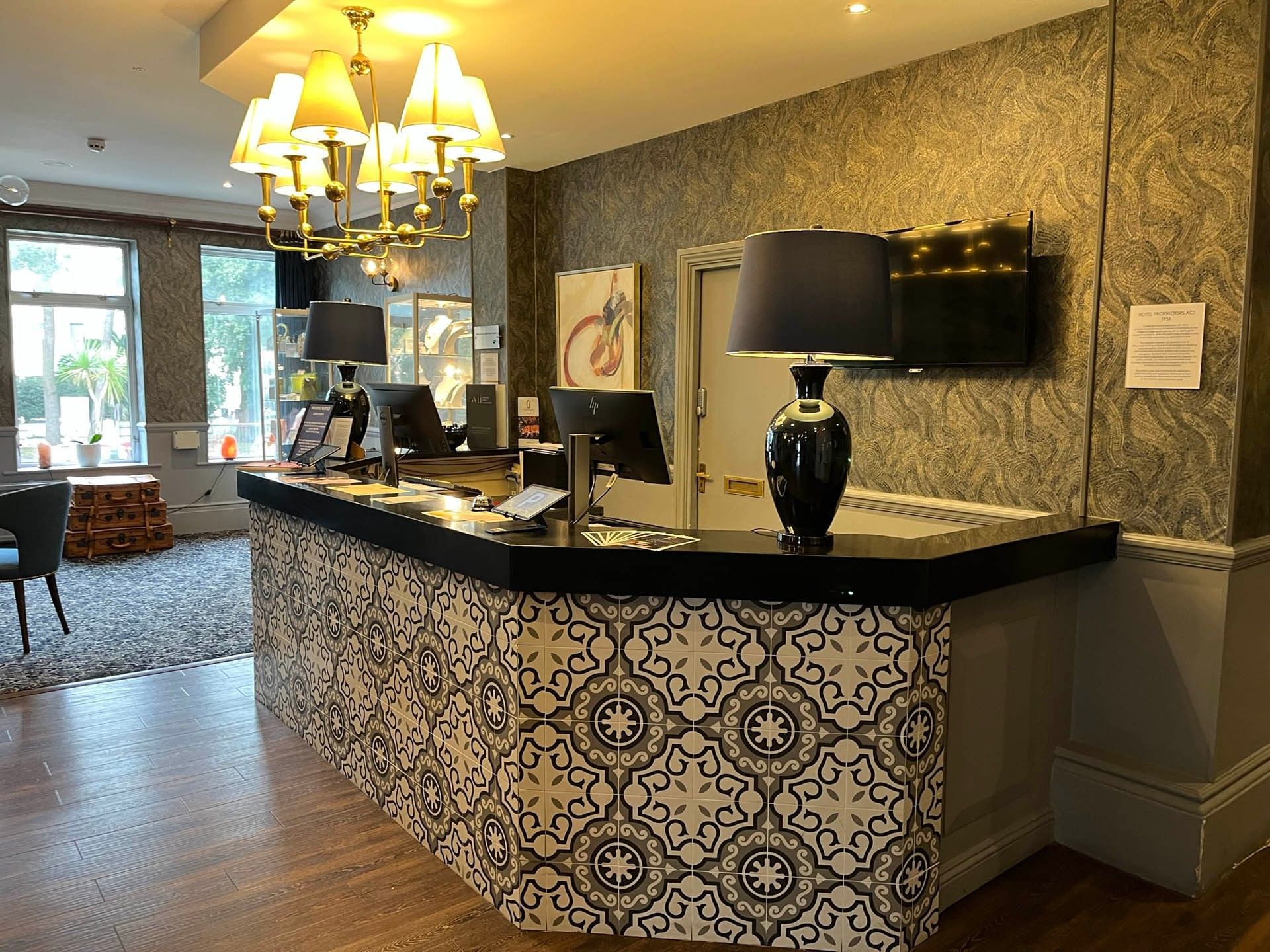 Hotel reception with patterned counter, monitors, lamps, and decorative elements in a warmly lit interior.