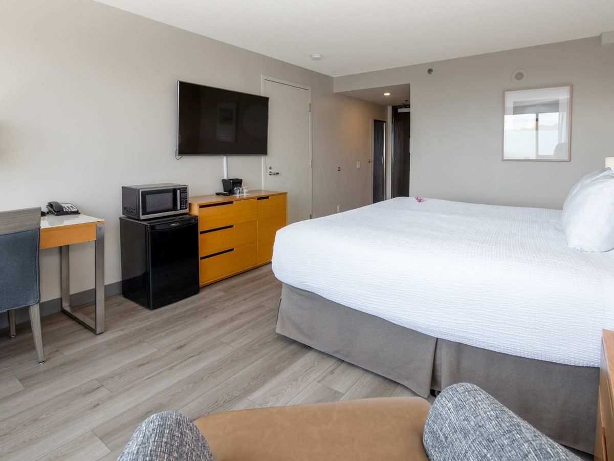 Hotel room with king bed, work desk, TV, mini fridge, microwave and armchair.