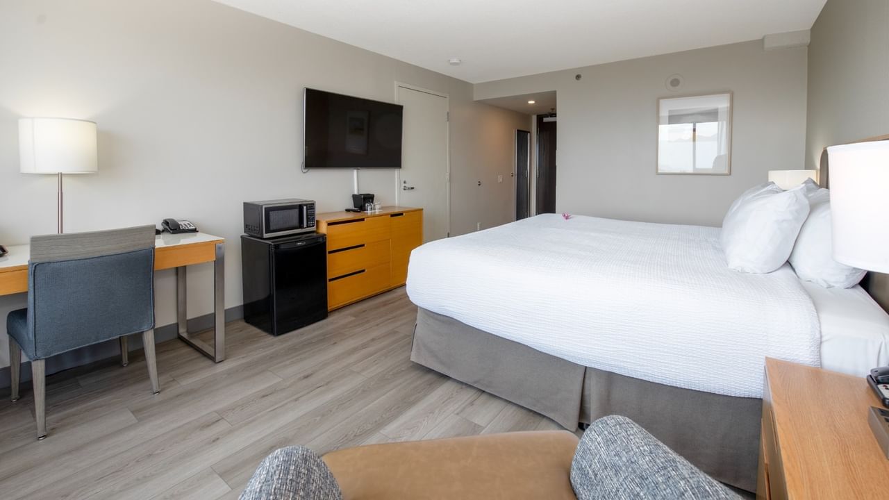 Hotel room with king bed, work desk, TV, mini fridge, microwave and armchair.