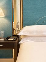 Dark wood nightstand by a white bed under a pleated lamp on a teal textured wall at Warwick Hotels & Resorts