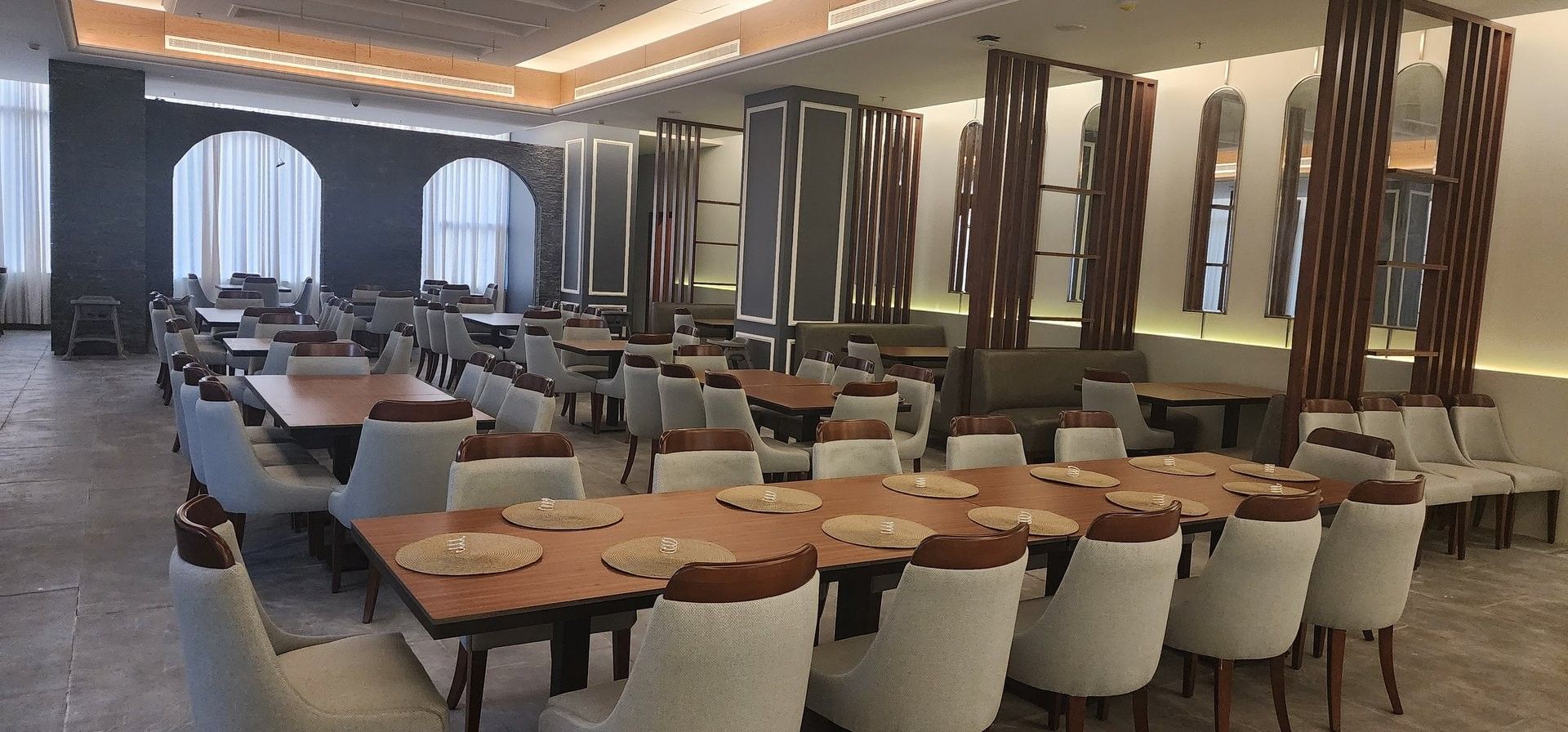 Almir Restaurant dining area with gray chairs by long wooden tables under a recessed ceiling at Warwick Jeddah Hotel & Spa