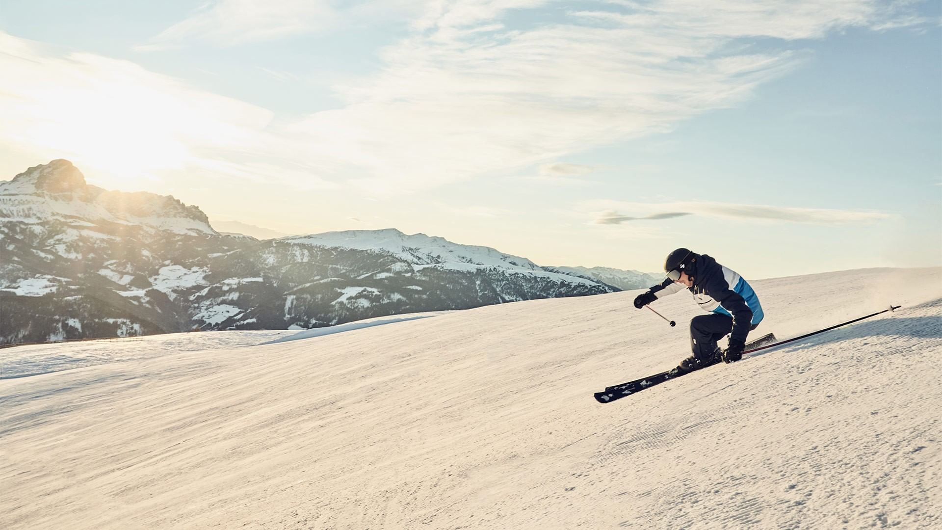 Sciatore in discesa su una pista innevata con montagne innevate sullo sfondo.