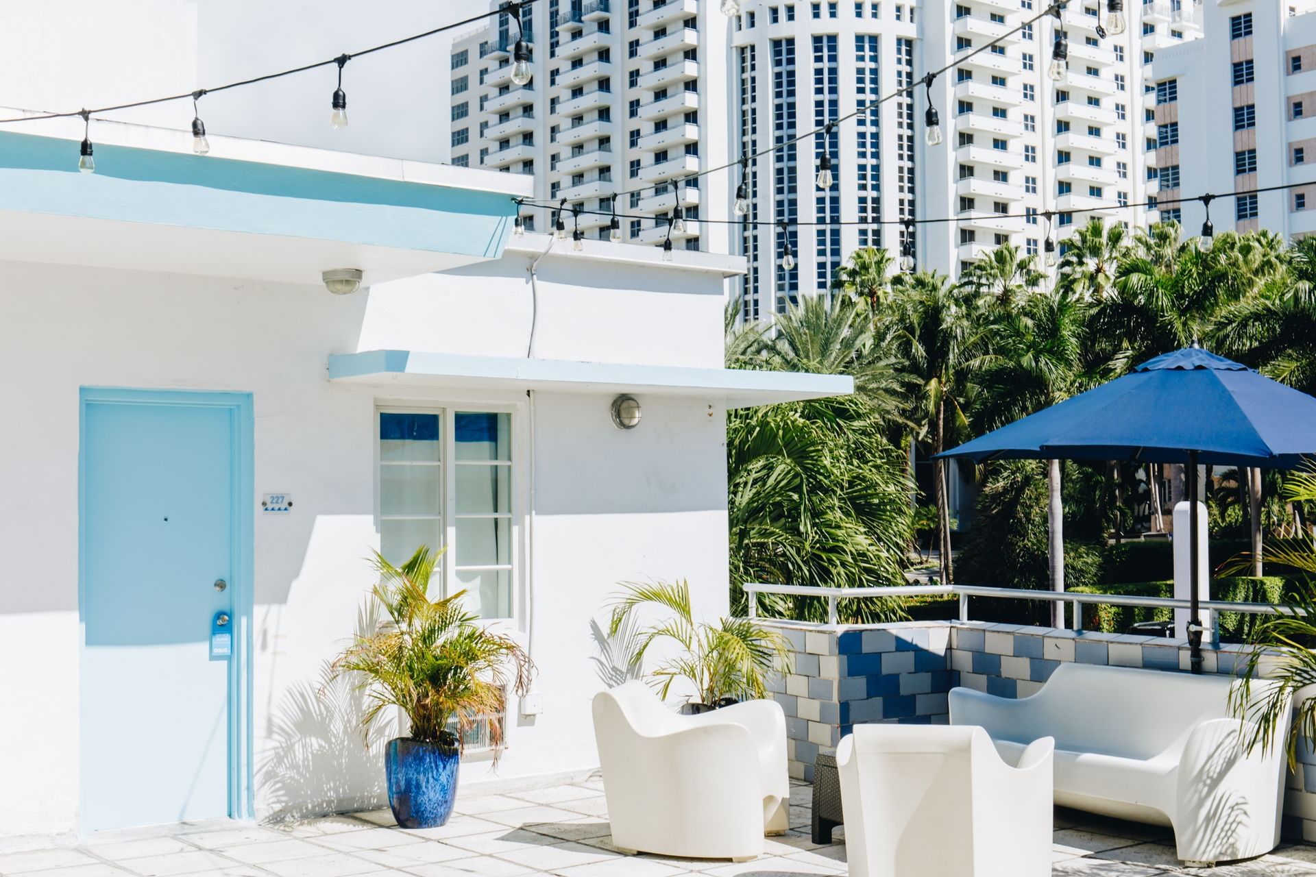 A white building with blue accents and outdoor seating area with furniture and plants.