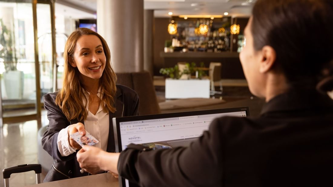 Guest receiving car parking information at Novotel Sydney Parramatta reception desk.
