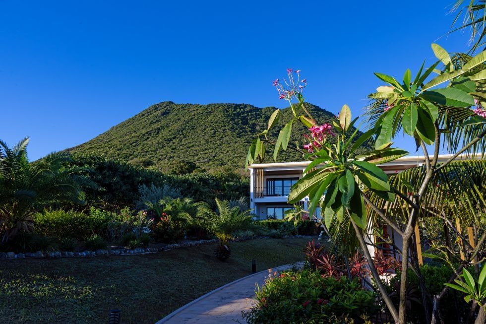Lush tropical garden surrounds a modern villa near Golden Rock Resort, with vibrant flowers and a scenic mountain backdrop
