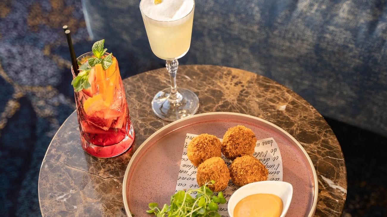 Croquettes with dipping sauce and two cocktails served on marble table in Cuvée at Sofitel Brisbane Central