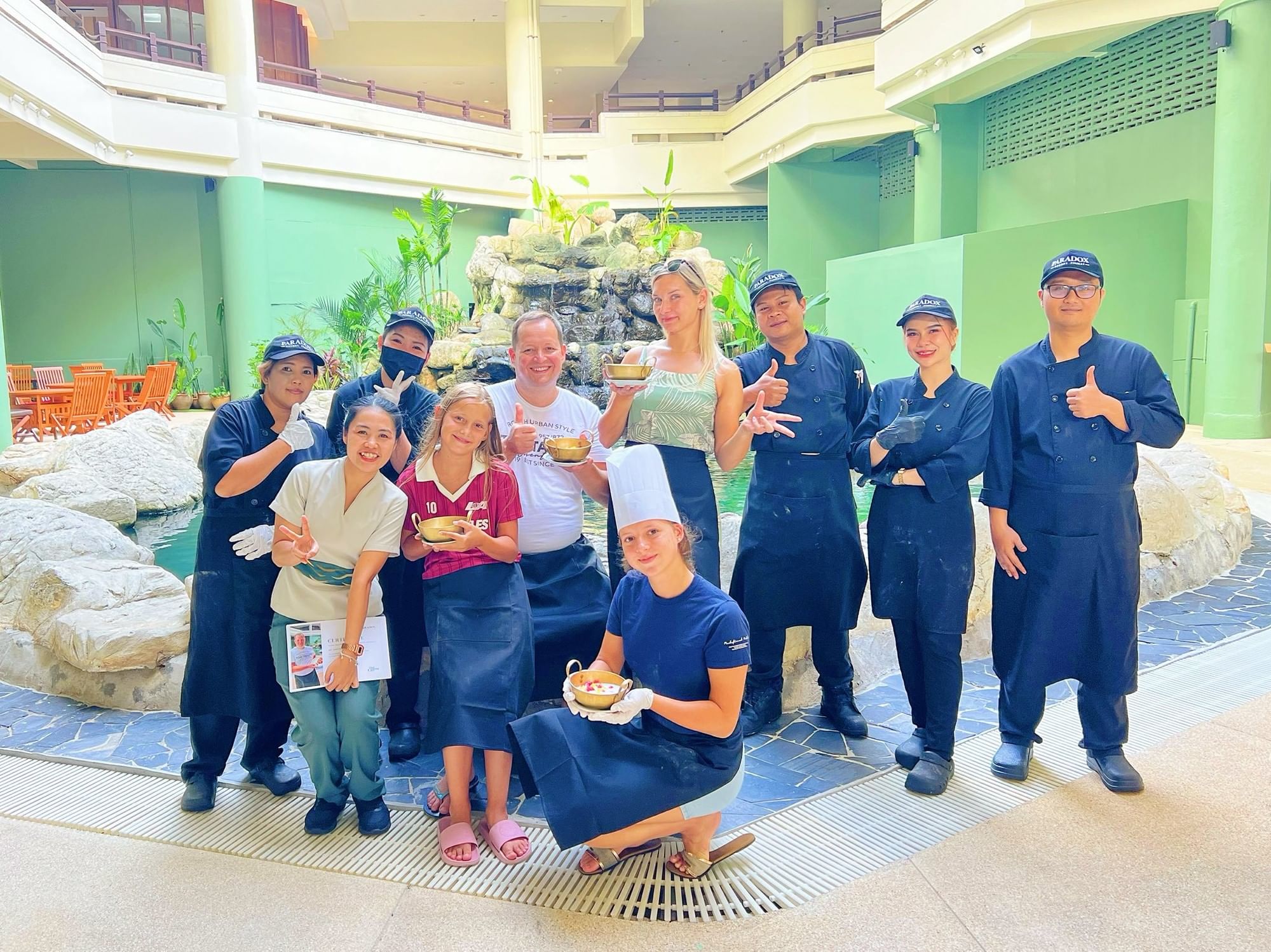 Guests and chefs smiling together after completing a Thai Cooking Class at Paradox Resort Phuket, a family-friendly hotel on Karon Beach.