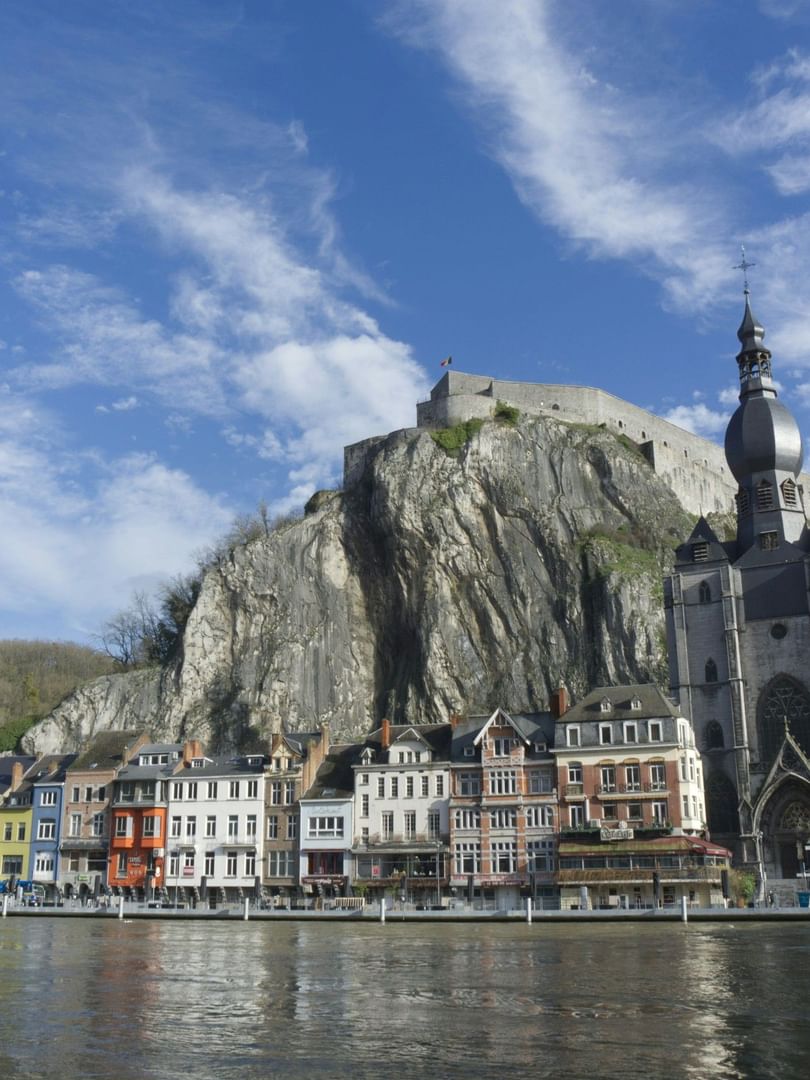 Vue panoramique d'une citadelle fortifiée dominant des maisons colorées au bord de la Meuse en Belgique sous un ciel bleu