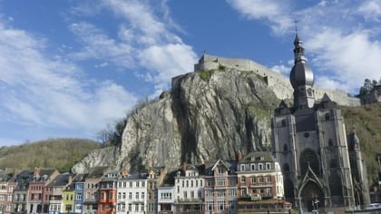 Vue panoramique d'une citadelle fortifiée dominant des maisons colorées au bord de la Meuse en Belgique sous un ciel bleu