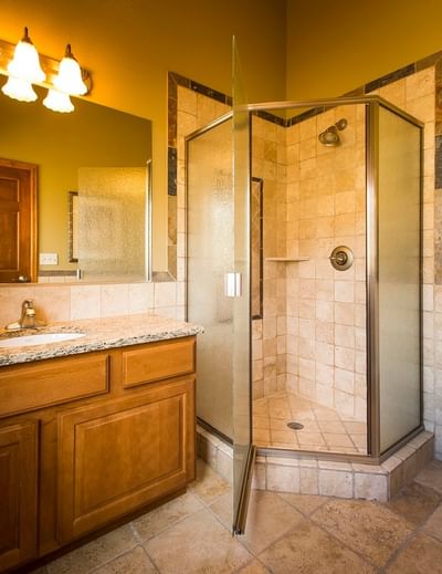 A rustic bathroom at The Stanley Hotel with a glass corner shower, a wooden vanity, and tiled walls and floors