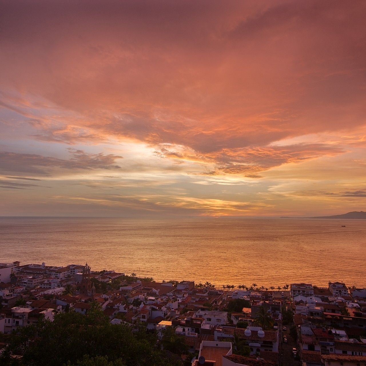 Sunset over the ocean and coastal Puerto Vallarta skyline from above in orange and pink hues.