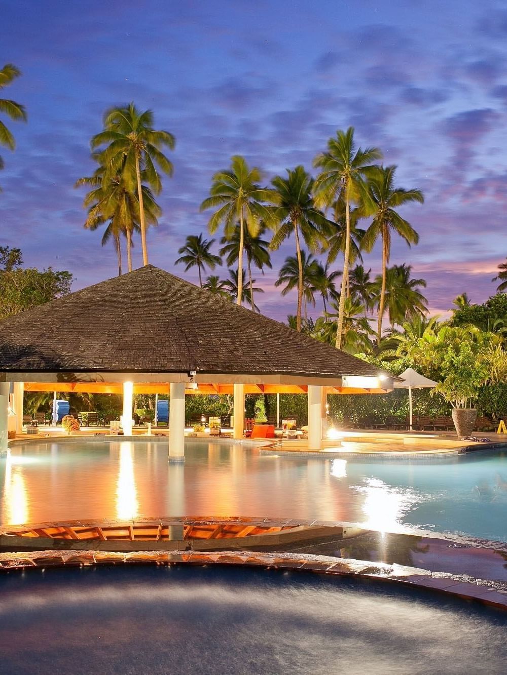 Exterior view of Nukunuku Restaurant & Bar with a hut by a swimming pool under palm trees and at The Naviti Resort - Fiji