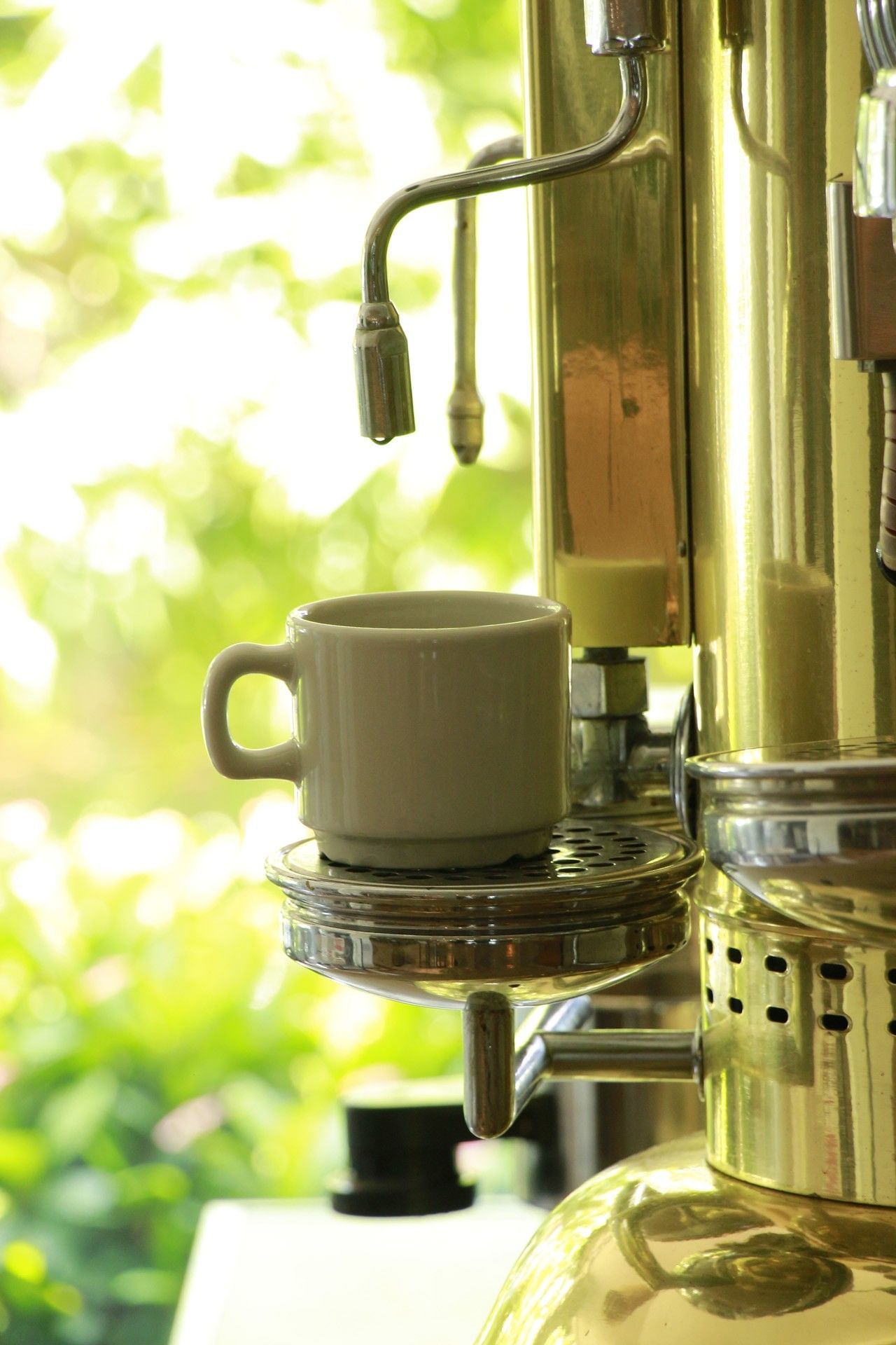 A small white espresso cup sits on a gleaming brass vintage coffee machine at the Country International Hotel restaurant