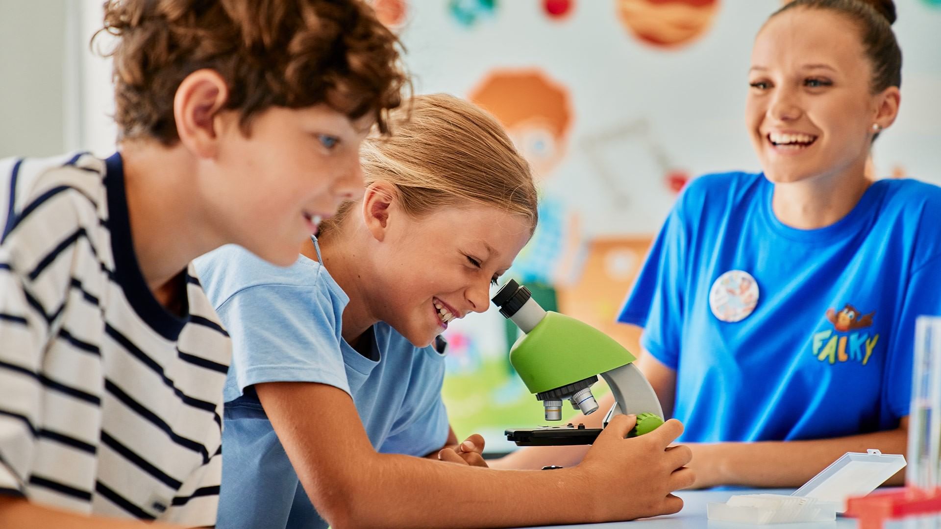Three kids with a teacher in a classroom looking through a microscope at Falkensteiner Family Hotel Diadora