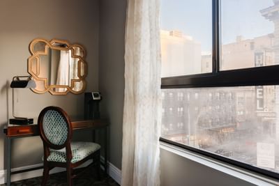 Wooden work desk with patterned chair and decorative mirror by window overlooking city street view at Hotel Bijou