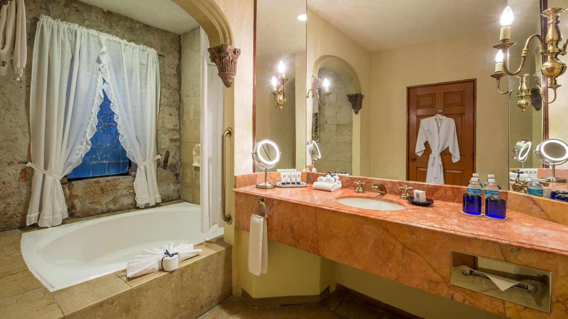 King Grand Class pink marble vanity with a large mirror and an arched stone bathtub at Quinta Real Aguascalientes