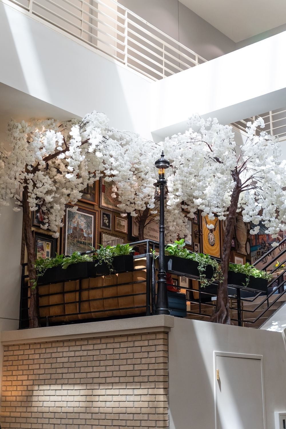 A lobby with artificial trees, a balcony, and framed pictures on the wall.