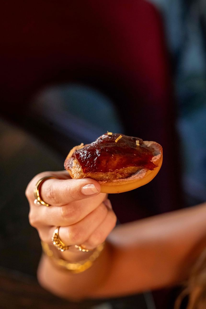 A person holding a Signature Roast Duck and Mantou Toast, a high tea offering available at Grand Orient Oriental High Tea.