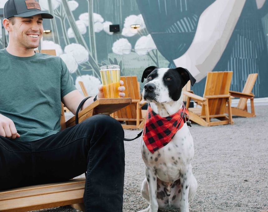 Man posing with his pet while having a drink at Kinship Landing