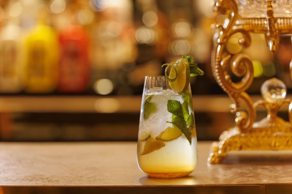 Iced mint cocktail with a lime wheel on a golden counter beside an ornate brass beverage dispenser at Polo Club Hotel