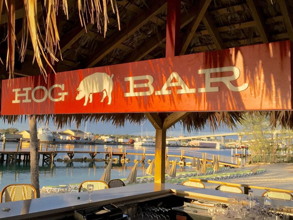 Hog Bar sign under a thatched roof by a calm bay and wooden pie at Warwick Paradise Island Bahamas