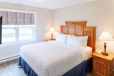 Bed with a high wooden headboard between two lit bedside lamps in Two-Bedroom Cottage at Rodd Crowbush Golf & Beach Resort