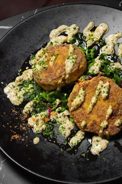 Two crispy golden patties on a bed of greens, drizzled with creamy sauce at Cypress & Oak Steakhouse, Frankfort
