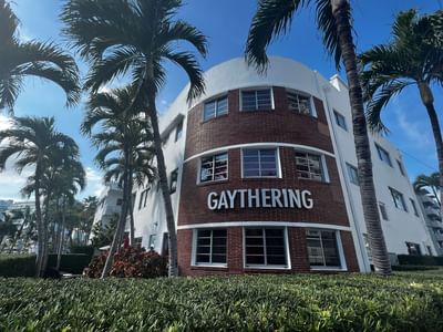 A brick hotel named The Gaythering with “GAYTHERING” on the building, framed by palm trees on a sunny day
