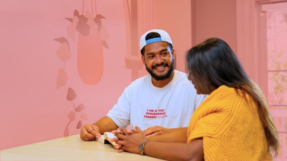 Man and woman sitting at a table, smiling and reading a book, at UniLodge Herston.