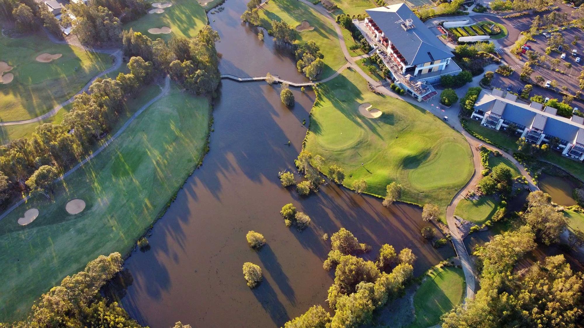 Aerial view of a golf course with a pond and adjacent buildings.