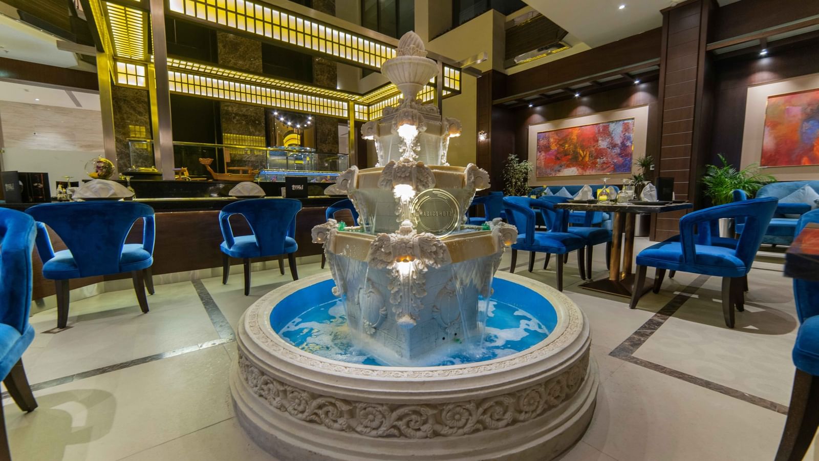 Ornate tiered water fountain by blue velvet chairs in Taki Restaurant lobby at Warwick Al Khobar