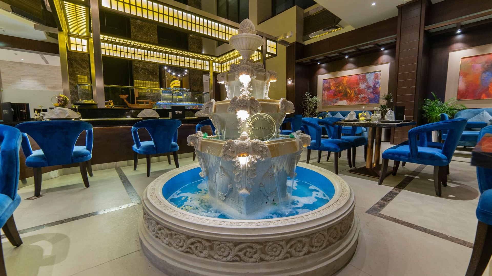 Ornate tiered water fountain by blue velvet chairs in Taki Restaurant lobby at Warwick Al Khobar