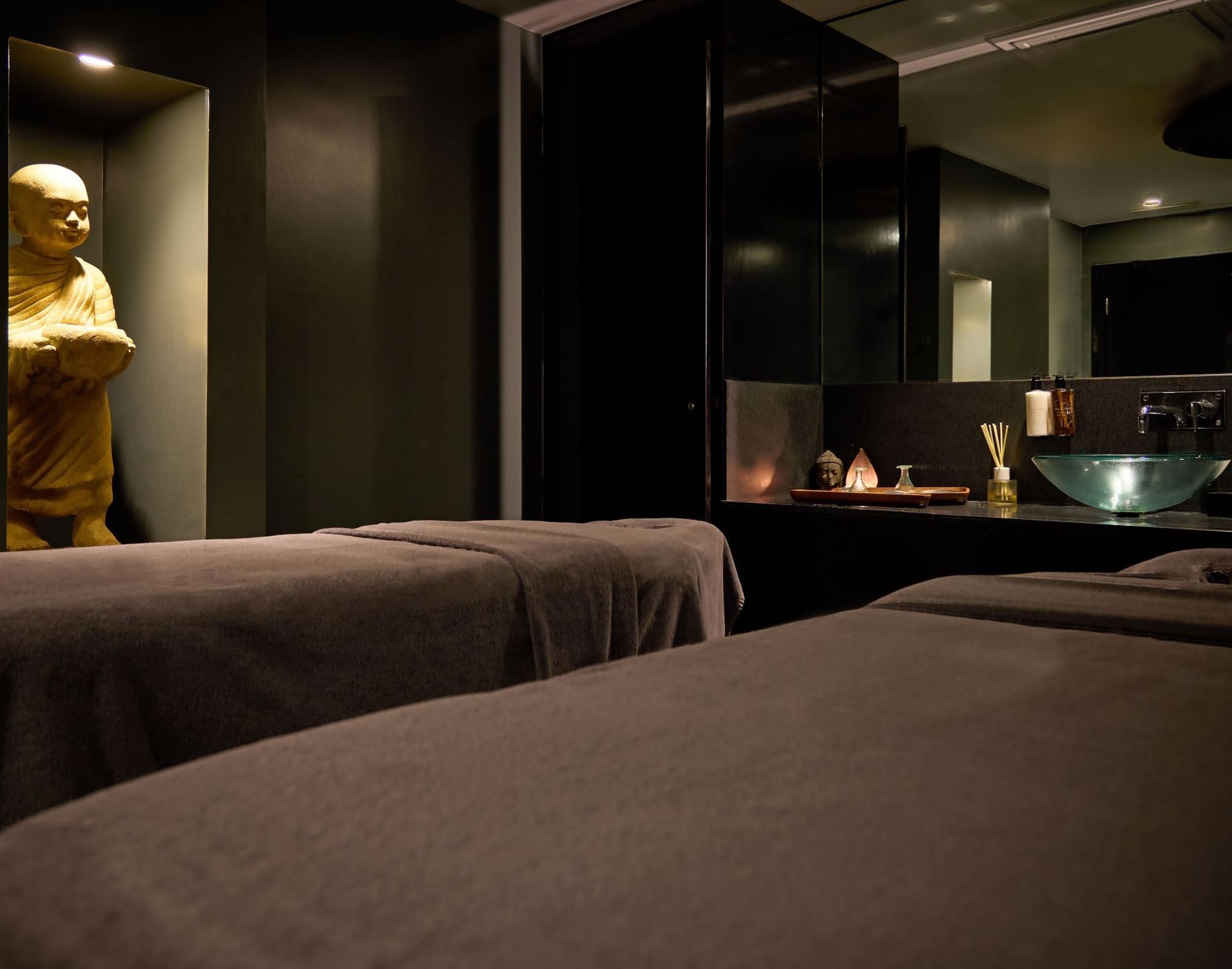 Two spa beds in a dark room with a golden Buddha statue at The May Fair Hotel.
