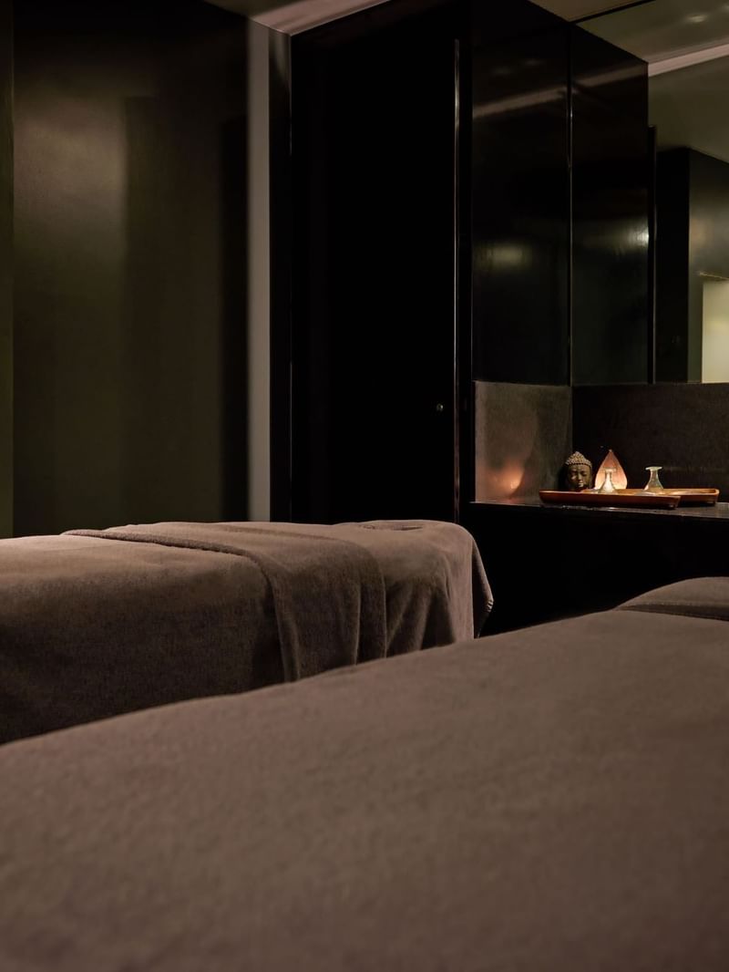 Two spa beds in a dark room with a golden Buddha statue at The May Fair Hotel.
