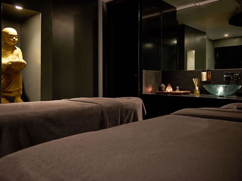 Two spa beds in a dark room with a golden Buddha statue at The May Fair Hotel.