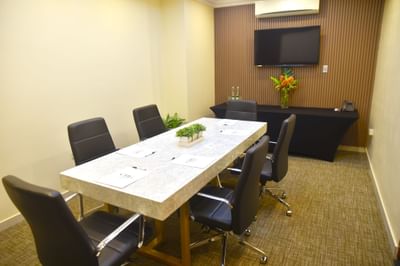 A conference room with a table, chairs & a TV in the Boardroom at Courtleigh Hotel & Suites