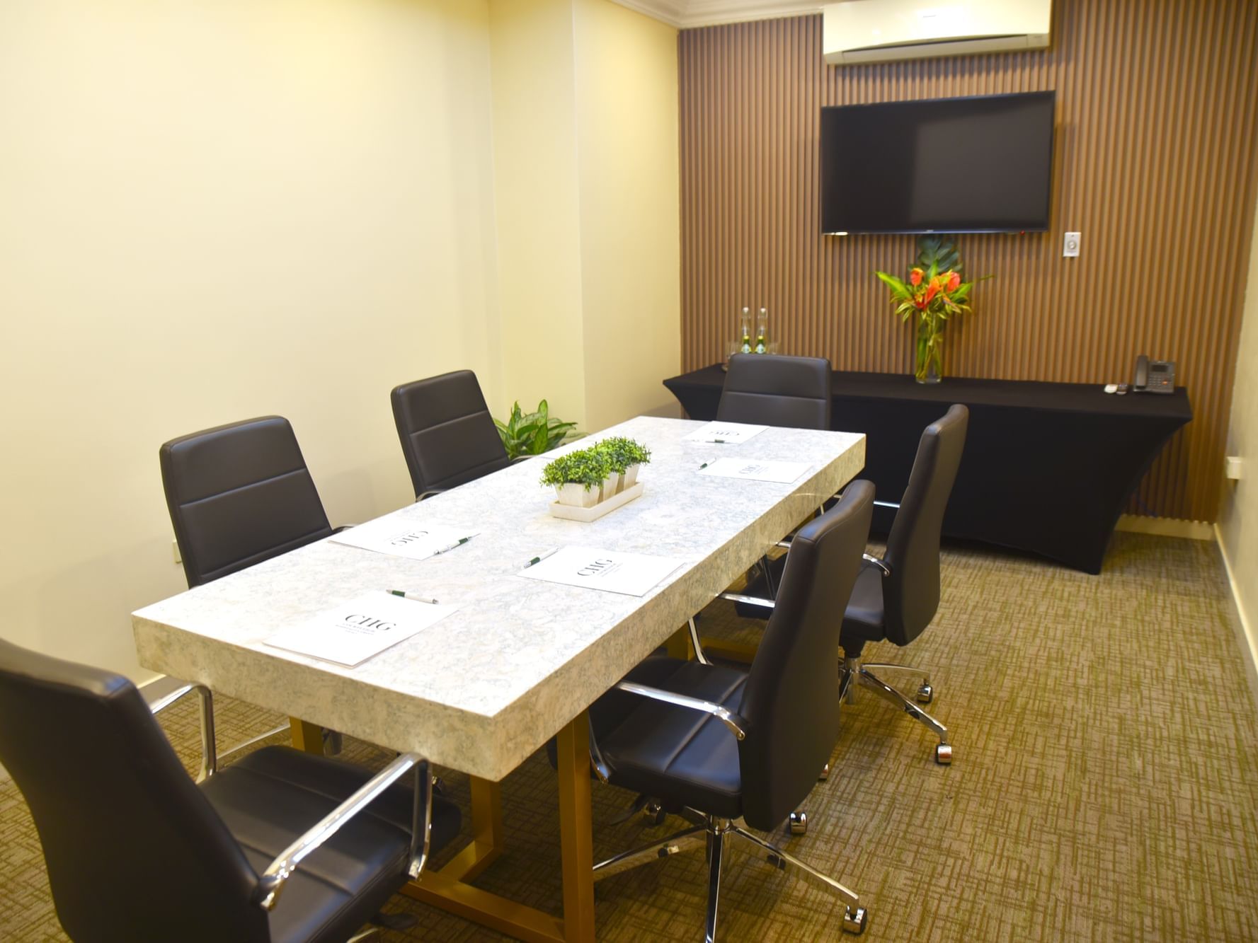 A conference room with a table, chairs & a TV in the Boardroom at Courtleigh Hotel & Suites