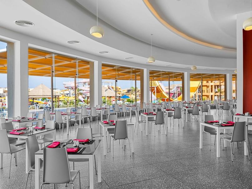 East & West Restaurant features modern dining space with gray chairs, red napkins, and pool views at Pickalbatros Villaggio Resort.