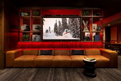 Matchstick Lounge cozy media room with brown couch and large screen showing skiers at Elevation Resort Spa