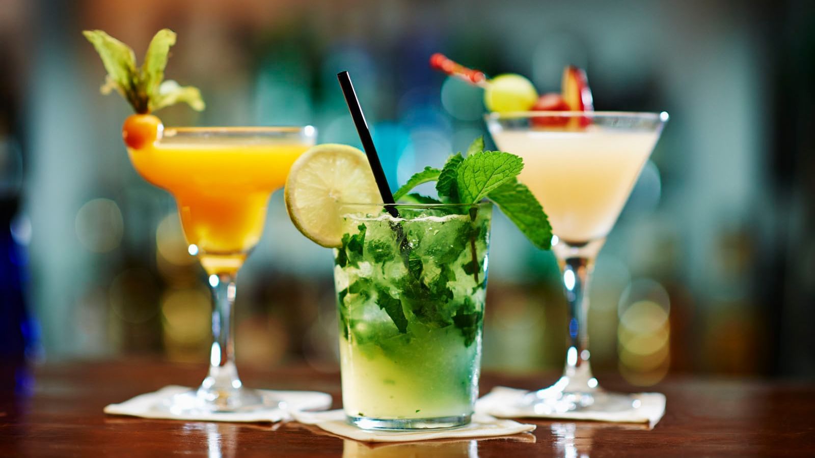 Three colorful cocktails, including a mojito, lined up on a dark, reflective wooden bar counter at the Marbella Club